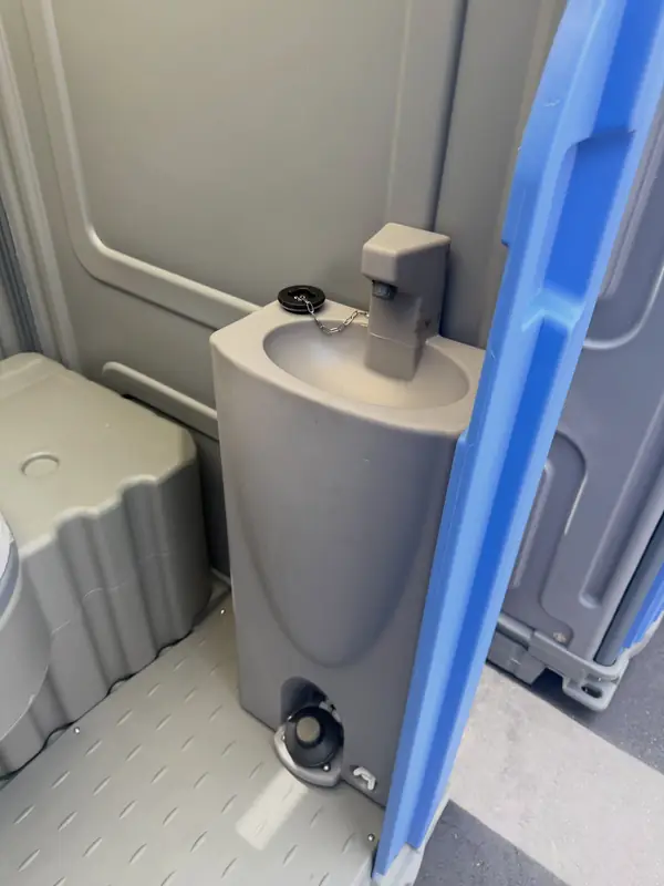 Inside a porta potty with a gray foot-pump sink beside the toilet