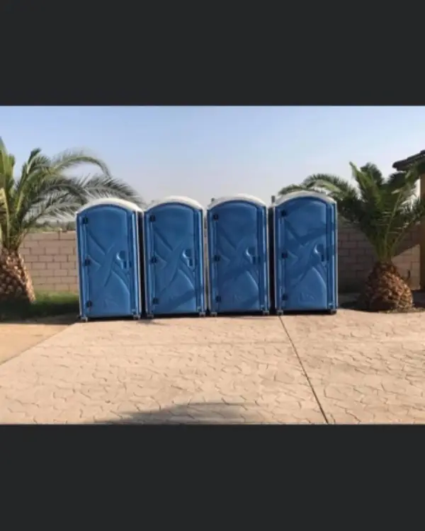 Four blue standard porta potties in a row on pavement
